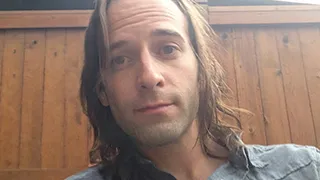 Stephen sitting outside, showcasing his shoulder-length hair